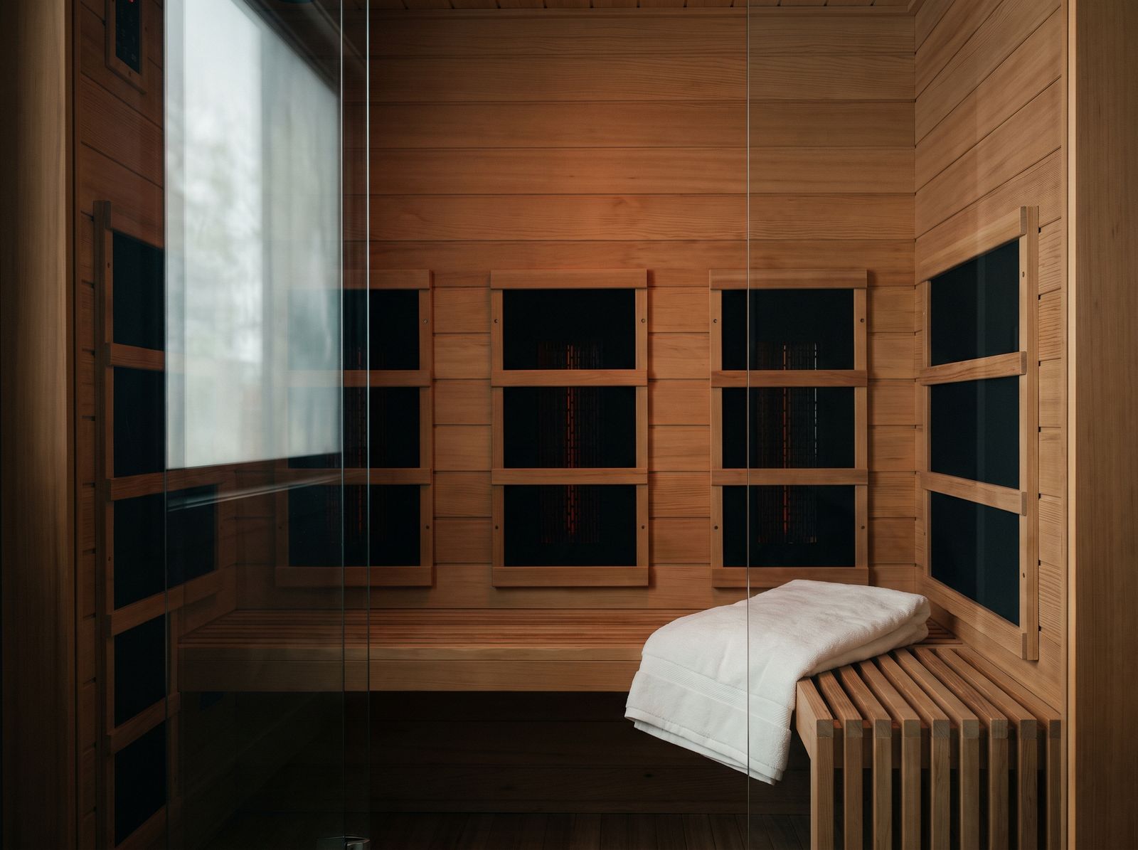 Infrared sauna interior in honey-toned hemlock with carbon heater panels and a glass door